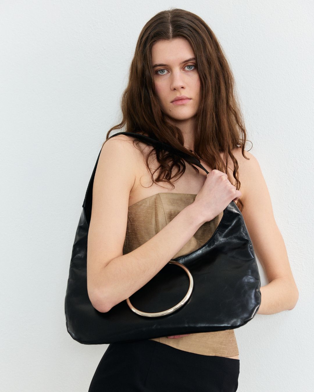 A woman holding a black shoulder bag with a soft texture and a signature metal circle closure.