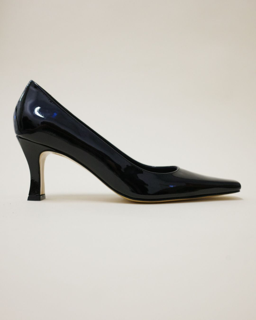 Black patent leather high heel shoe on a light beige background