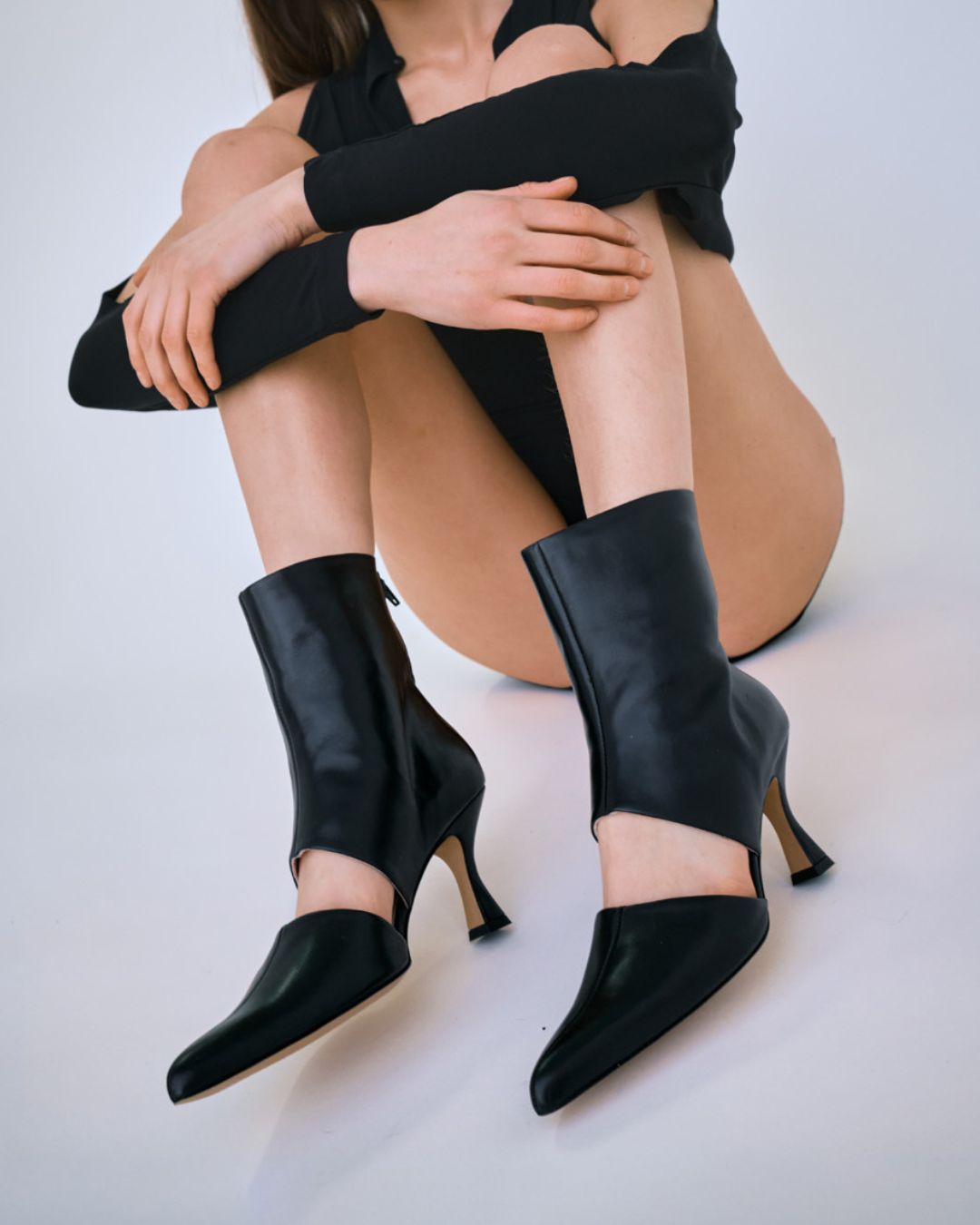 KALDA black leather pointy toe ankle boots with a cut-out detail on a person